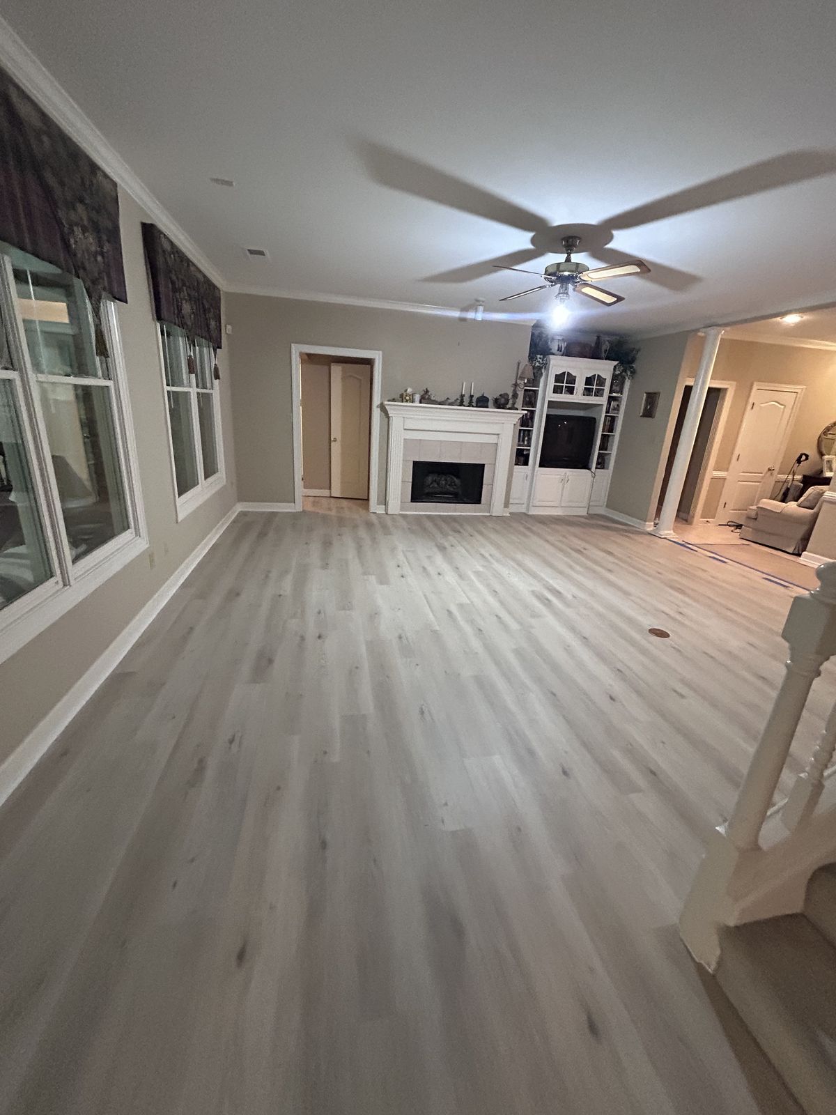 Newly installed light plank-style flooring in a large living room with a fireplace and ceiling fan