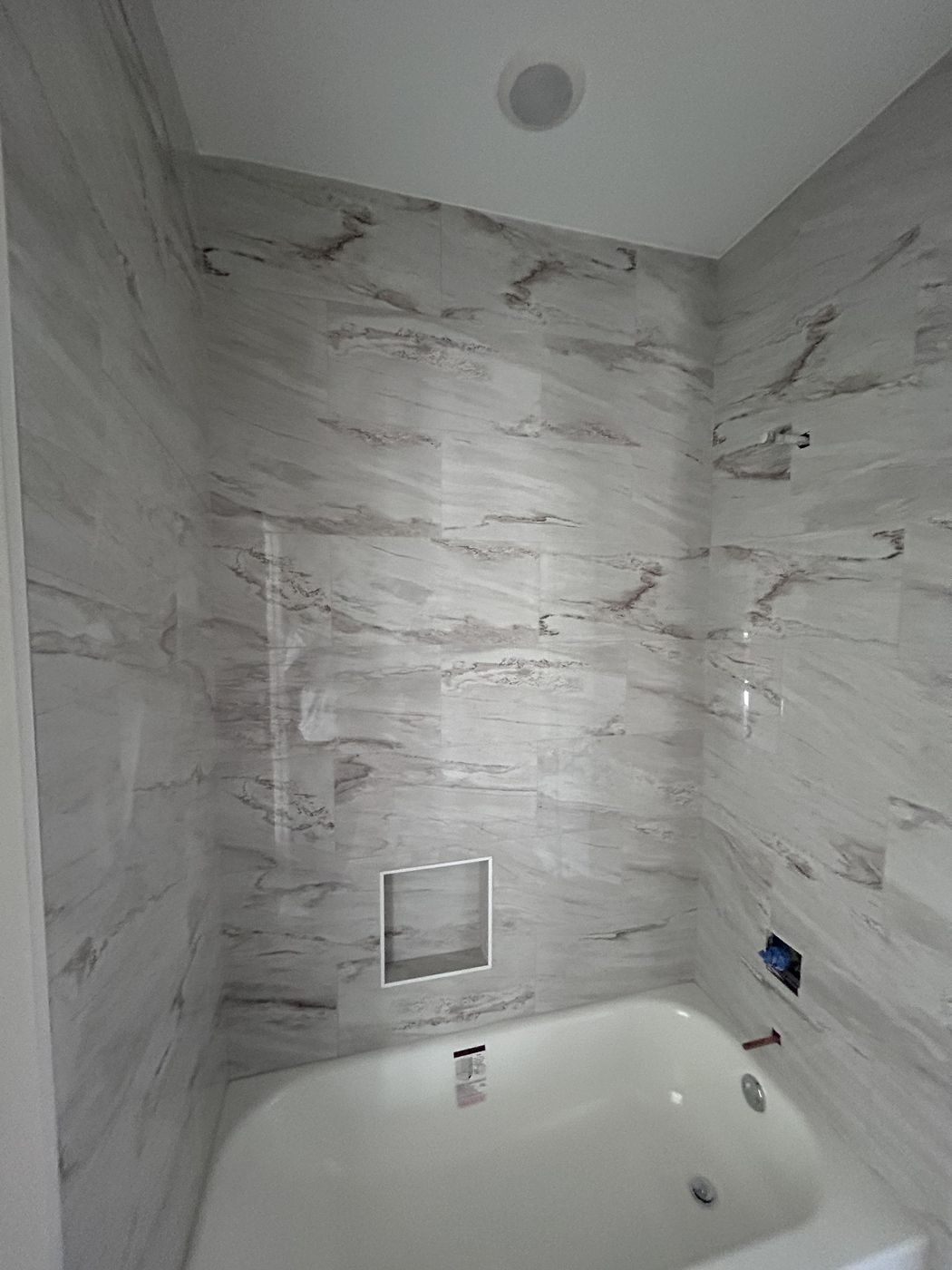 Bathtub with a floor-to-ceiling marble-look tiled shower surround and a recessed niche